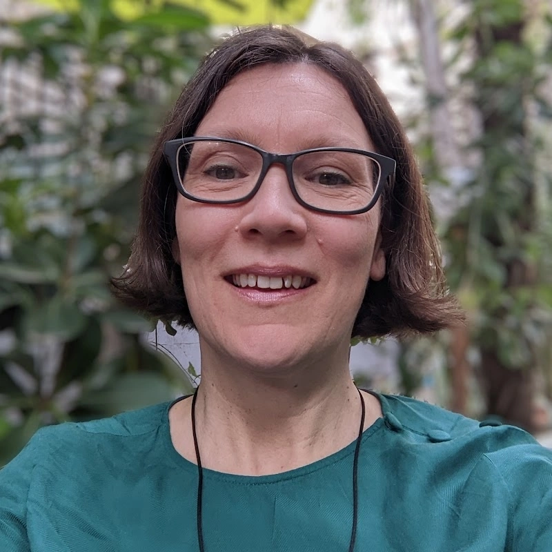 A smiling woman with glasses taking a selfie outdoors